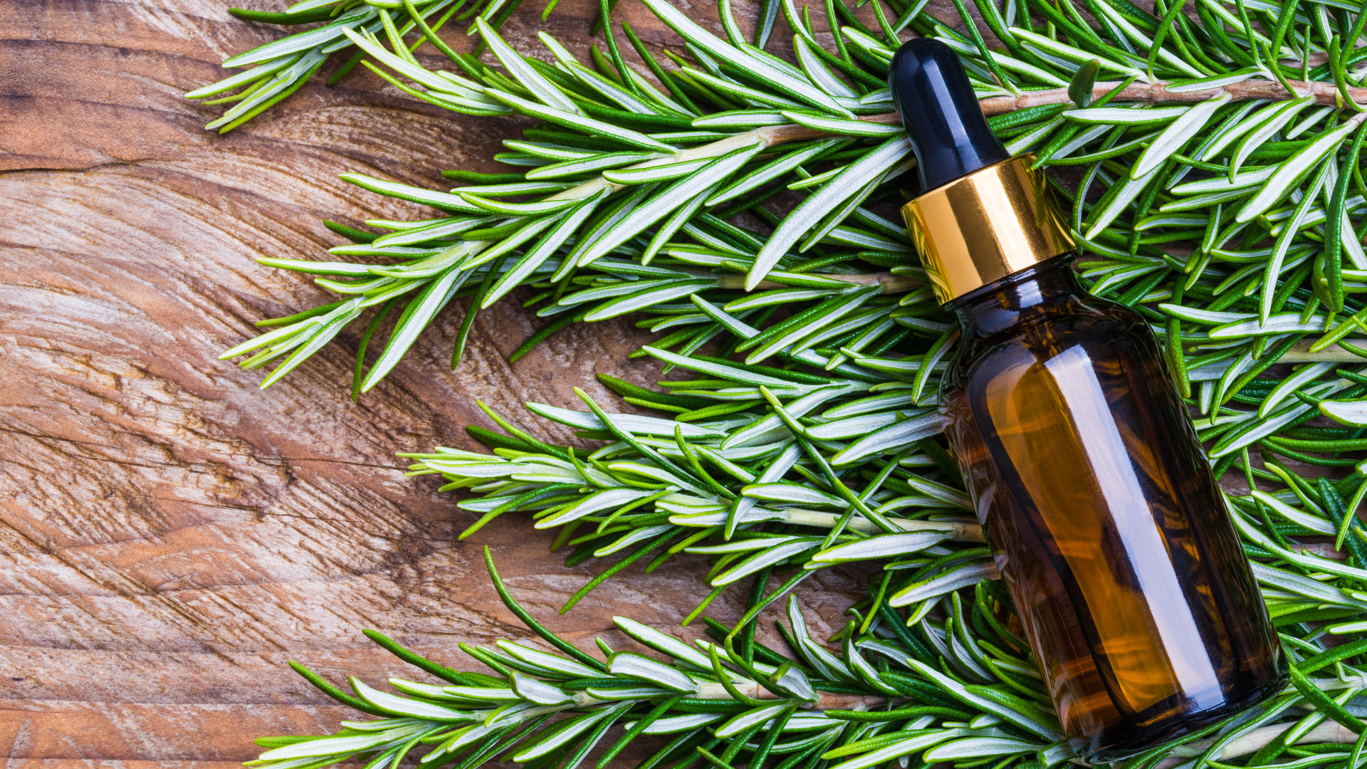 rosemary leaves on and a bottle of rosemary oil on a wooden top